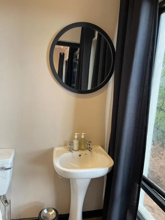 Pedestal sink with round mirror and dark curtain in bright bathroom