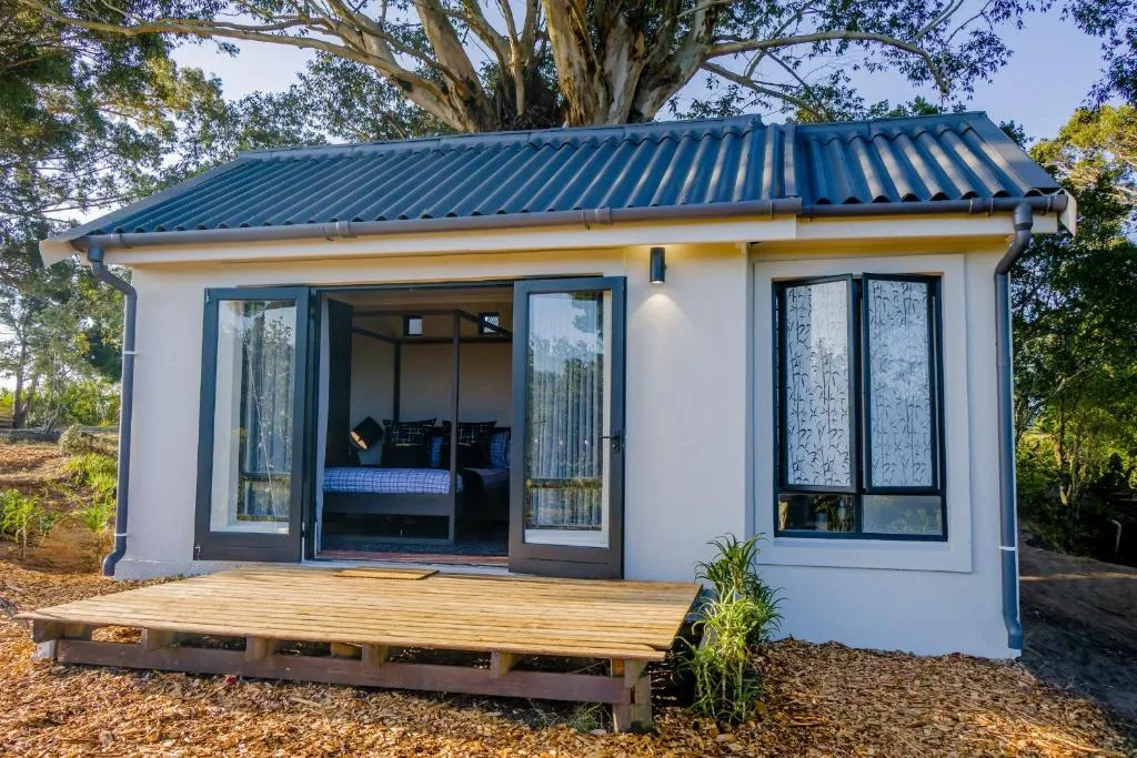 White cottage with blue roof and wooden deck surrounded by trees