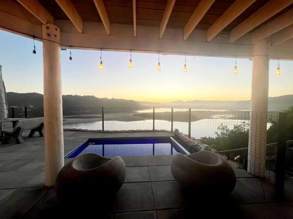 Covered deck with pool, hanging lights, and lagoon sunset views