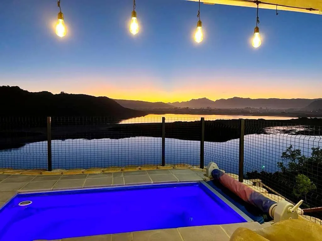 Illuminated pool overlooking lagoon at sunset with mountain backdrop
