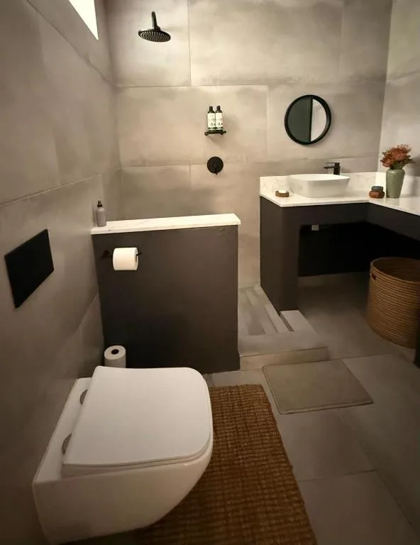 Modern bathroom with toilet, basin, rainfall shower, and round mirror