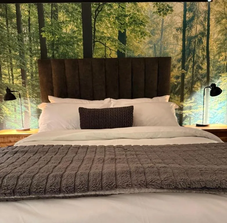 Modern bedroom with forest view, dark headboard, white linens, and black bedside lamps
