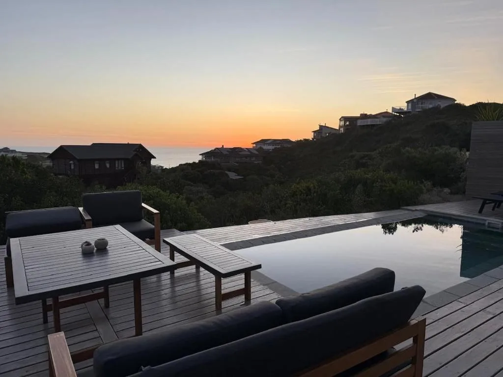 Wooden deck with infinity pool overlooking ocean at sunset