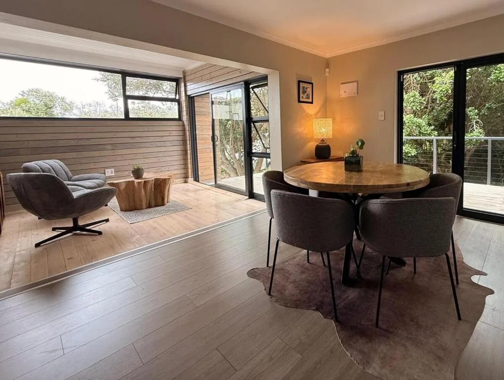 Modern dining area with round wooden table and black chairs overlooking gardens