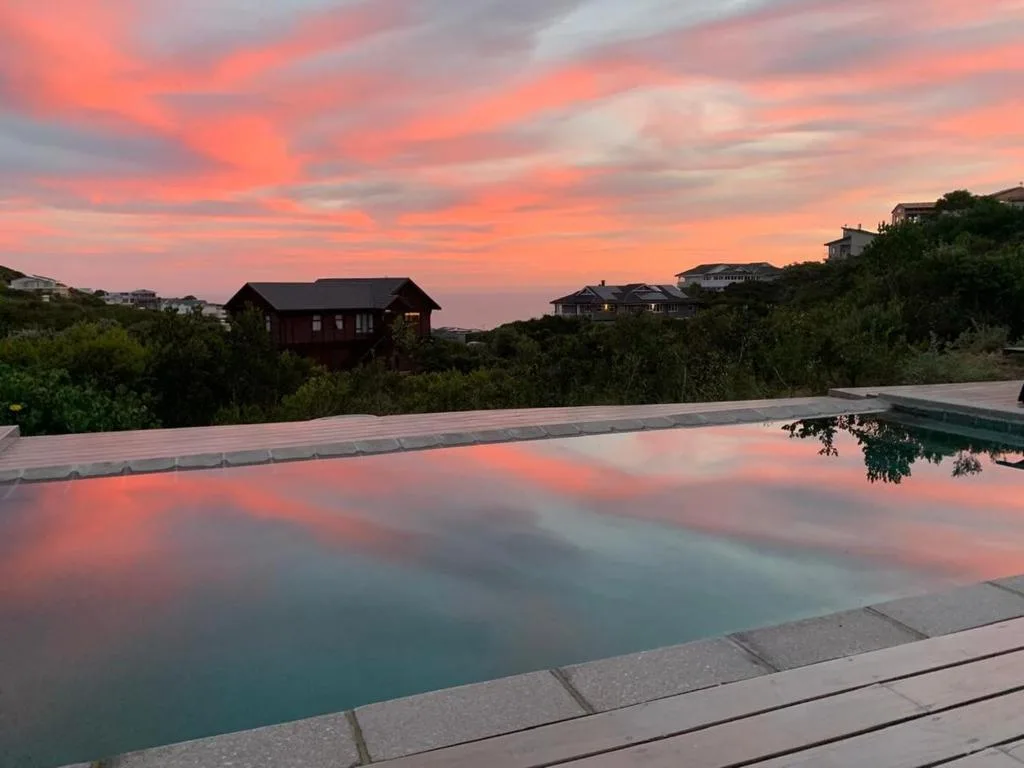 Infinity pool at sunset with dramatic pink sky and surrounding homes