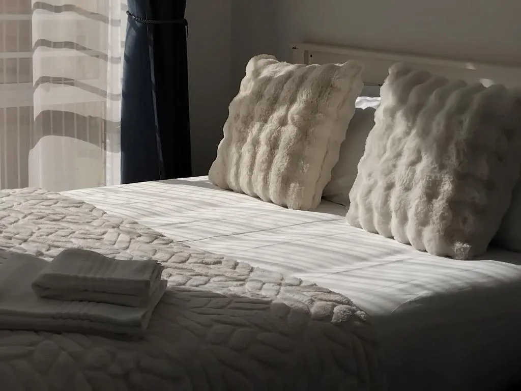 Bed with white linens and decorative textured pillows near window