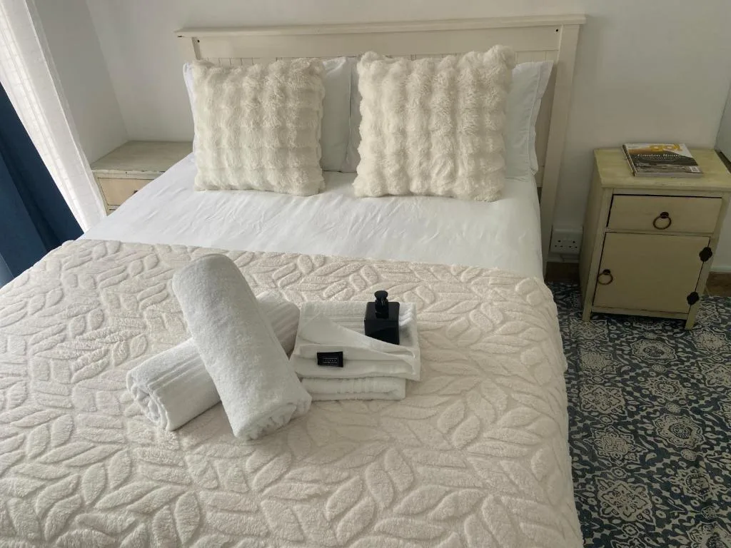 Neatly made bed with white linens and fluffy cushions, beside table