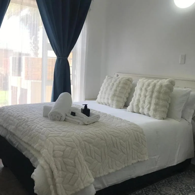 Bright bedroom with queen bed, cream bedding, decorative pillows, and blue curtains
