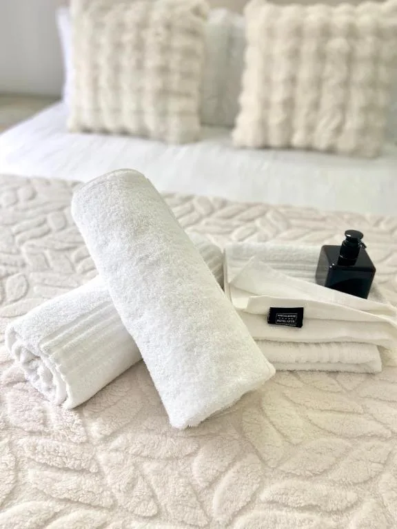 Rolled white towels with toiletries on bed, luxury welcome amenities