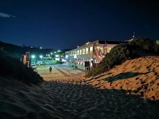 Beachfront building lit at night with sandy beach in foreground