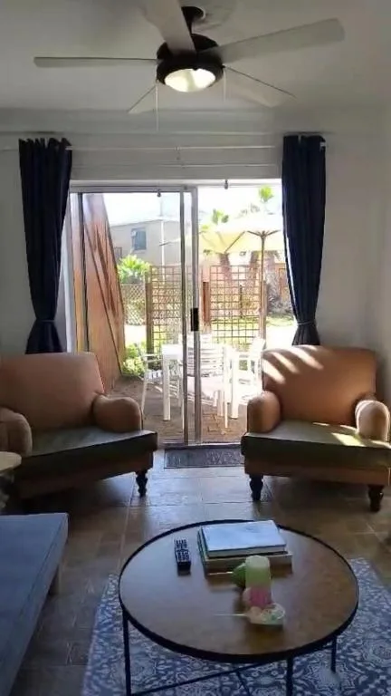 Bright lounge with tan armchairs, round coffee table, ceiling fan, garden views