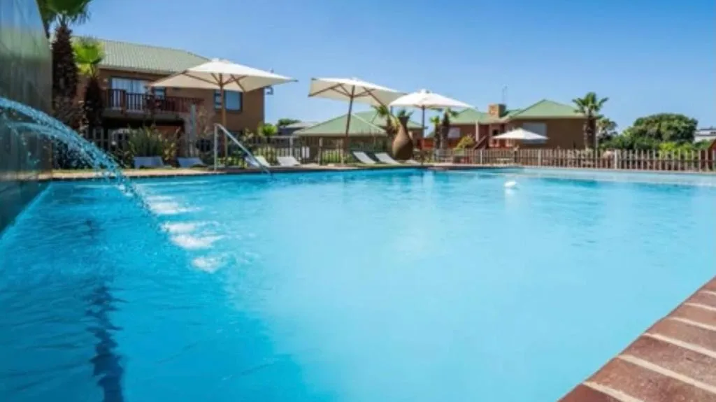 Sparkling blue swimming pool with shade umbrellas and wooden deck loungers