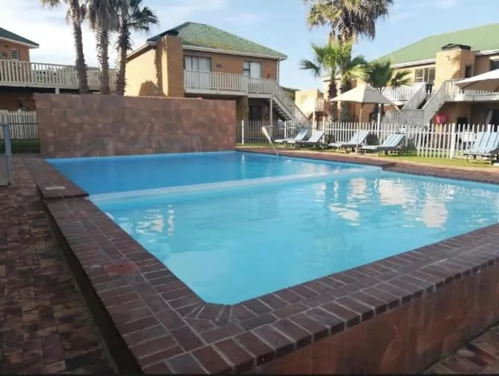 Bright blue swimming pool with brick surround and beachfront properties visible