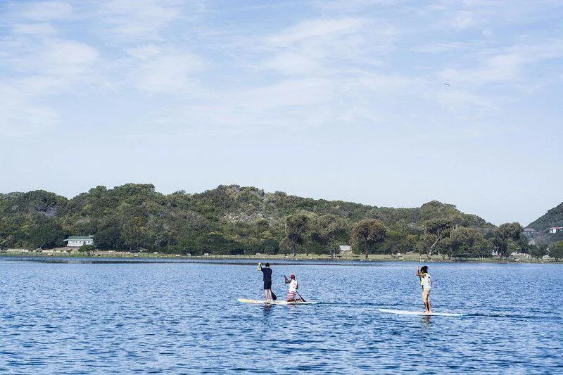 Scenic lagoon view with paddle boarders and forested hills beyond