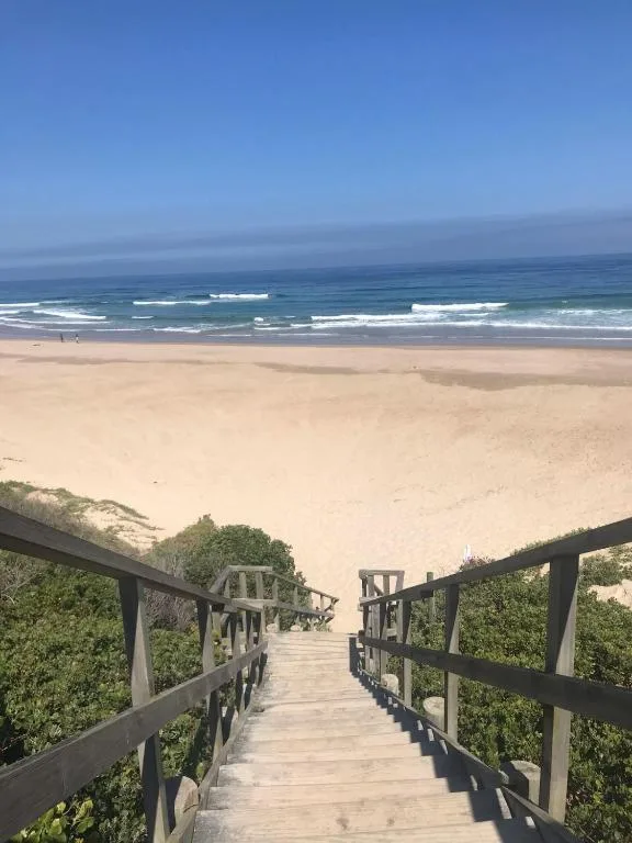 Wooden boardwalk descending to pristine beach with rolling ocean waves