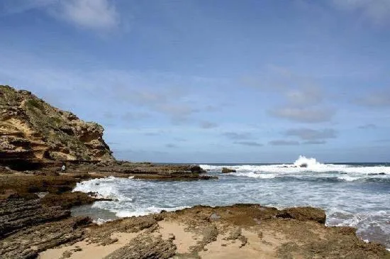 Rocky coastline with sandy beach and crashing ocean waves under blue sky