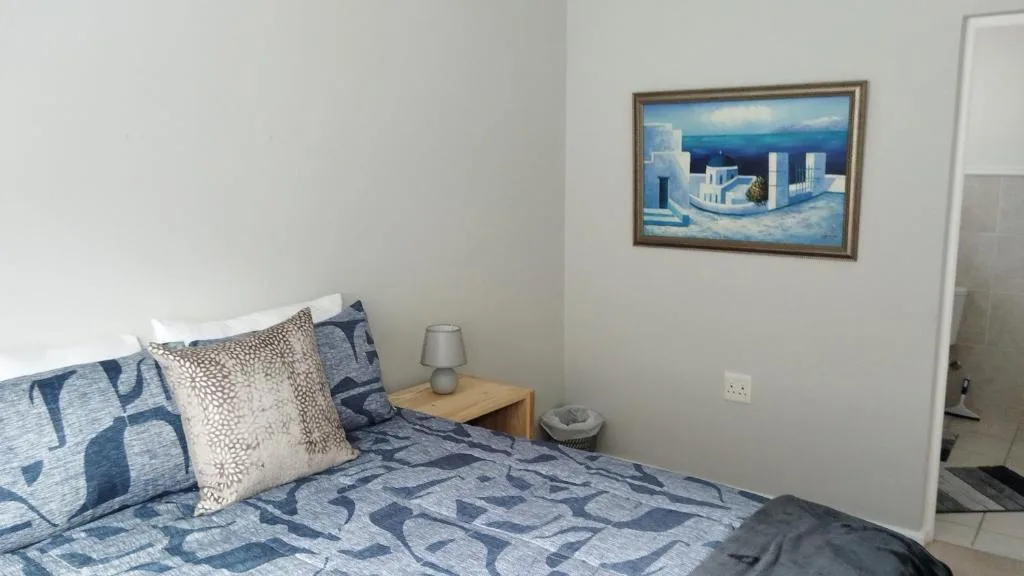Bedroom with blue patterned bedding, cushions, and coastal artwork on wall