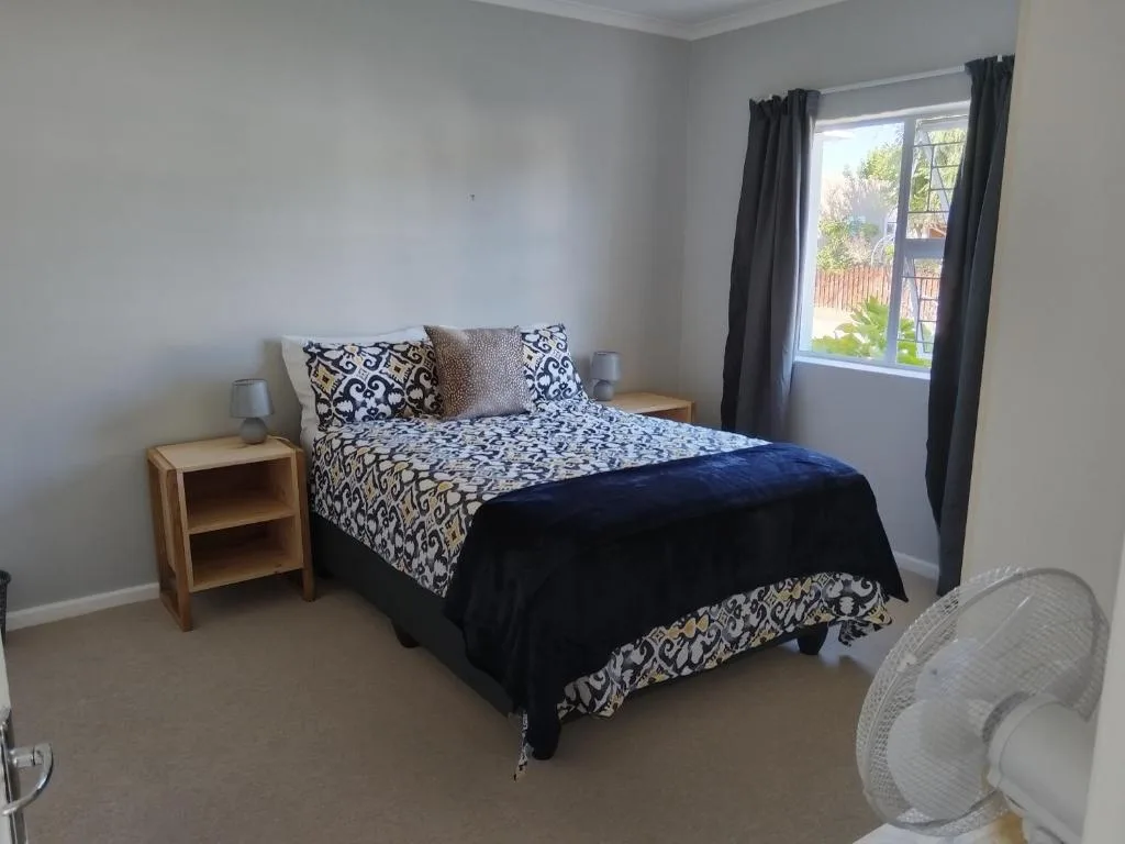 Bright bedroom with patterned bedding, wooden nightstand, and garden view window