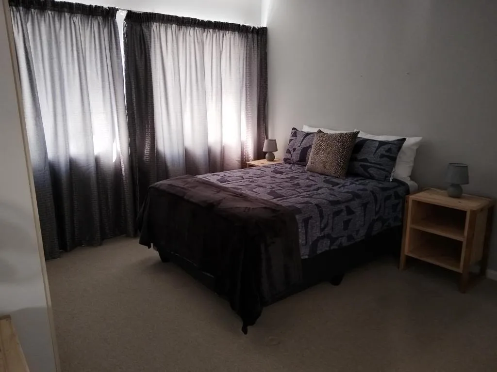 Spacious bedroom with queen bed, dark bedding, decorative pillows, and large windows with flowing curtains