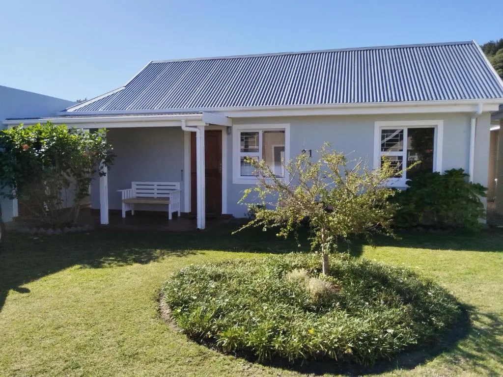 White cottage with corrugated metal roof and manicured garden landscape