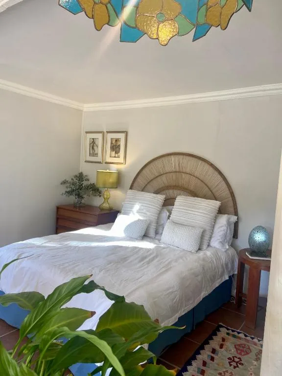 Bright bedroom with woven headboard, white bedding, and artistic ceiling fixture