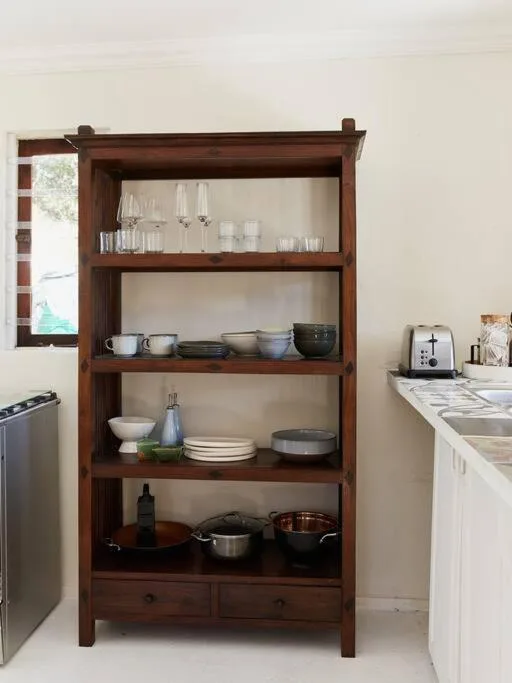 Wooden open shelving unit displaying kitchenware, glassware, and cooking equipment