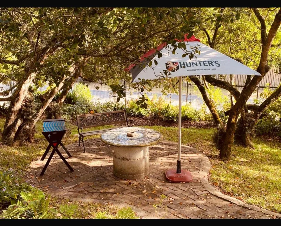 Shaded outdoor braai area with circular stone table and umbrella seating