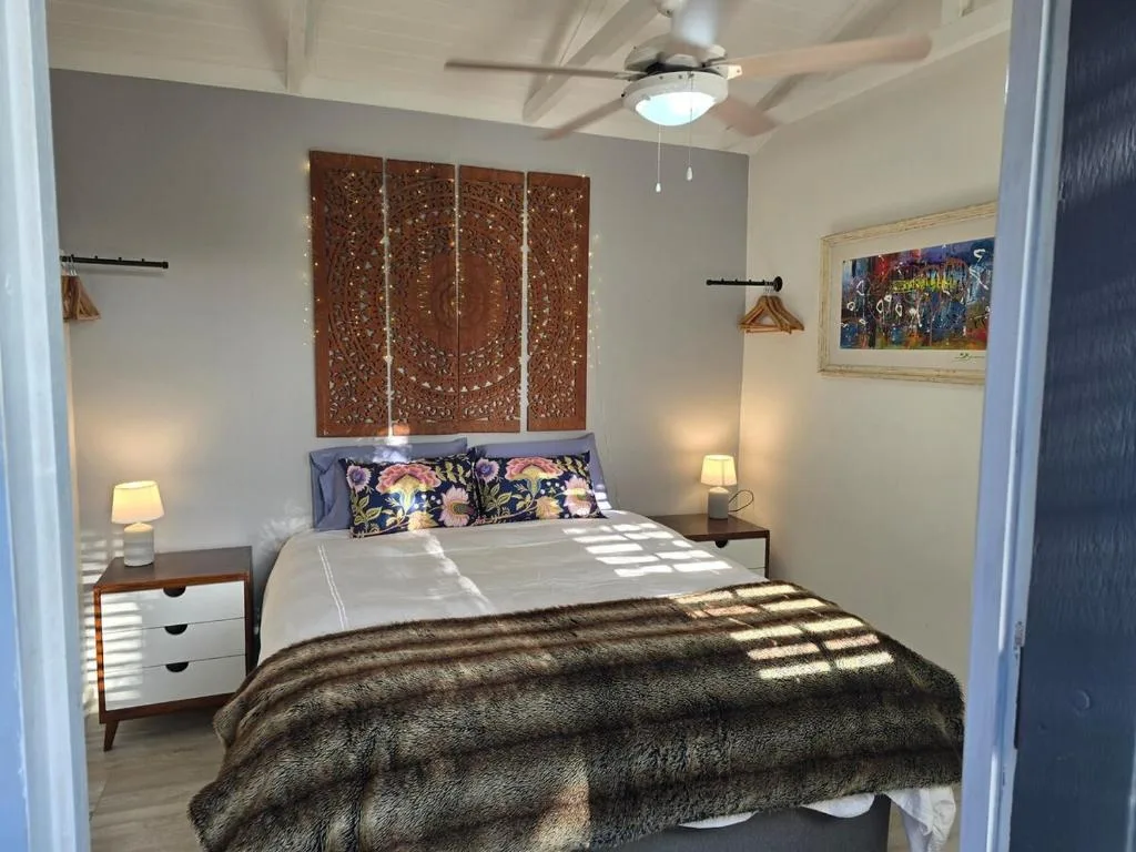 Bright bedroom with queen bed, wooden headboard art, and ceiling fan