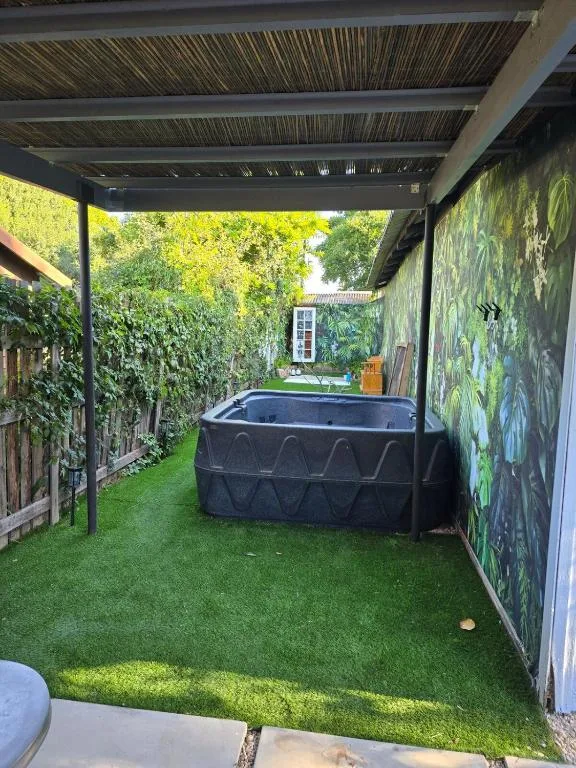 Covered outdoor deck with artificial turf, hot tub, and lush green surroundings