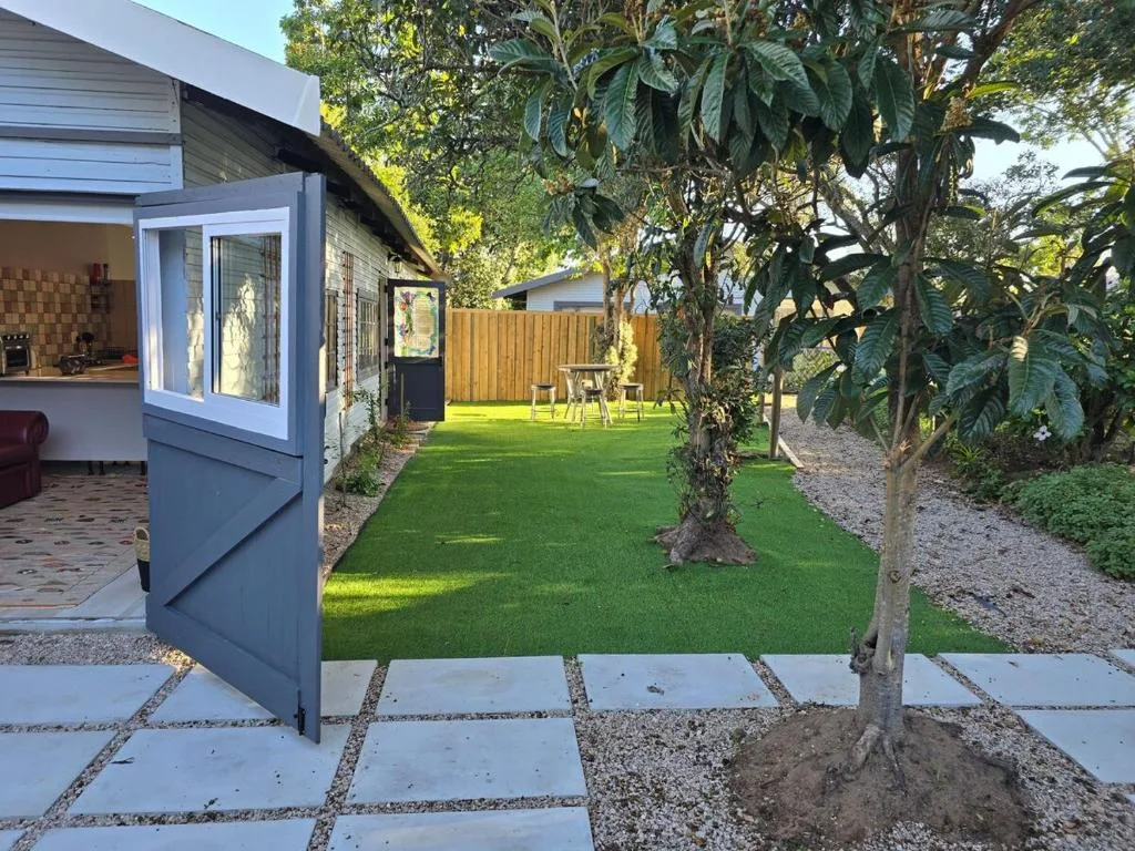 Modern cottage exterior with lush green lawn, mature trees, and paved pathway