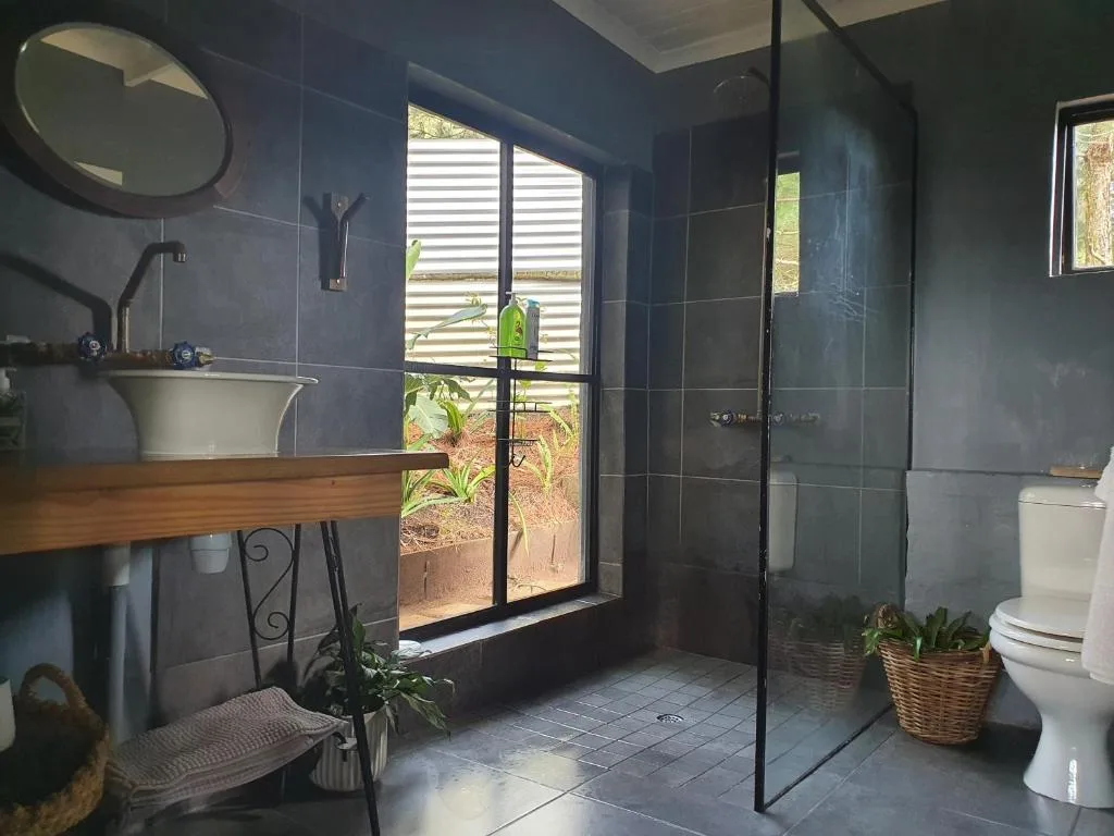 Modern bathroom with dark tiling, wooden vanity, circular mirror, and garden views