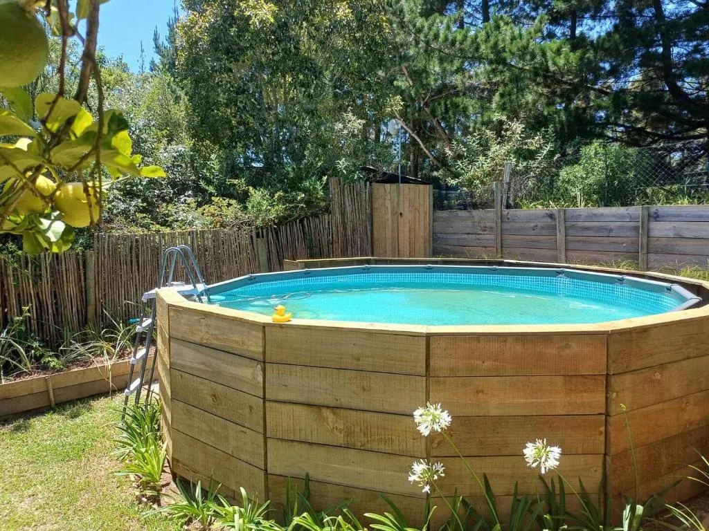 Circular above-ground pool with blue water in fenced garden surrounded by trees