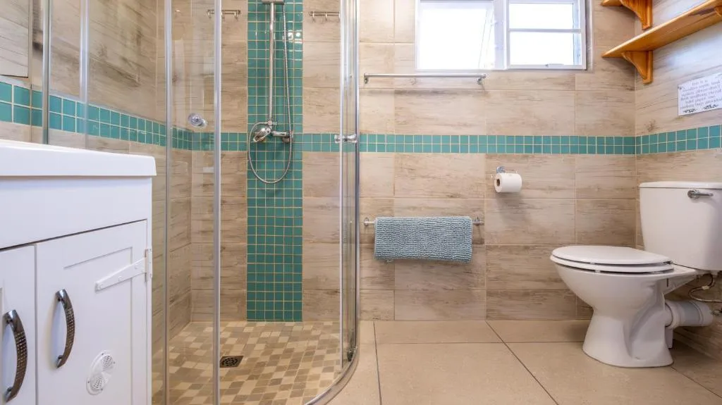 Modern bathroom with walk-in shower, vanity, toilet, and green tile accent