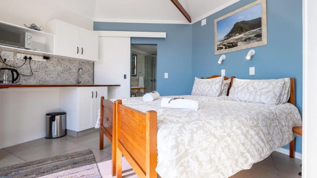 Bright bedroom with wooden bed frame and white bedding, blue walls, kitchenette