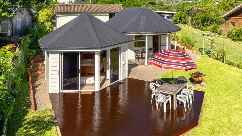Dark wooden deck with outdoor seating, striped umbrella, and manicured garden surroundings