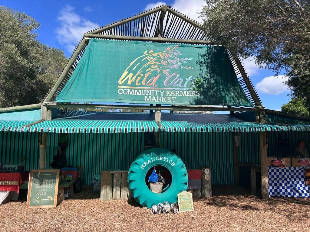 Green corrugated iron building with Wild Oat Community Farmers Market signage and turquoise decorative tire