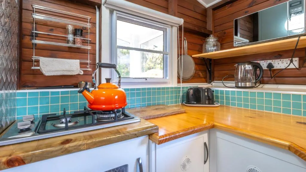Bright kitchen with turquoise tiles, wooden counters, orange kettle, and open shelving