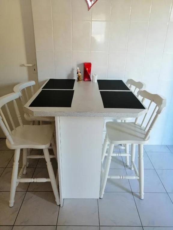 White dining table with black placemats and four white wooden chairs