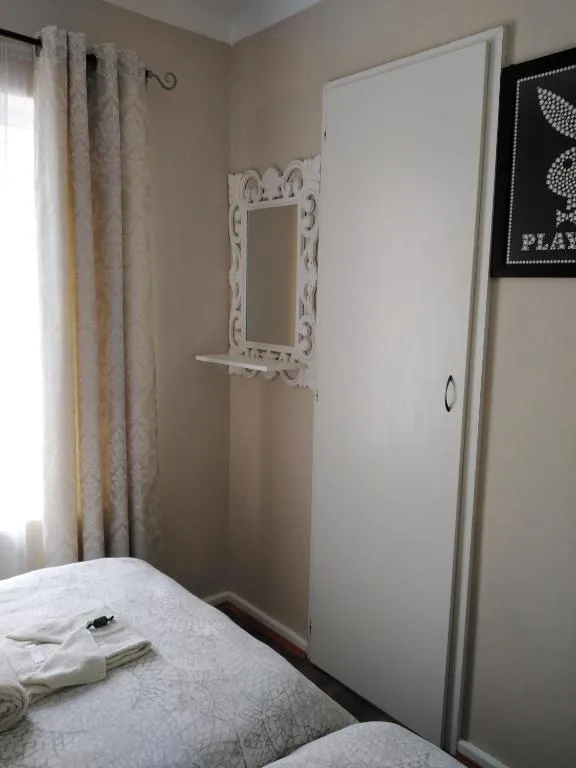 Bedroom with white bed, cream curtains, and decorative mirror on wall