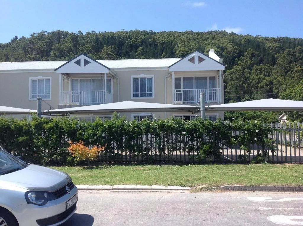 Modern white holiday home with gabled roof and deck awnings, forested backdrop