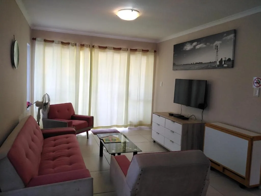 Spacious lounge with burgundy sofas, wall-mounted TV, and glass coffee table