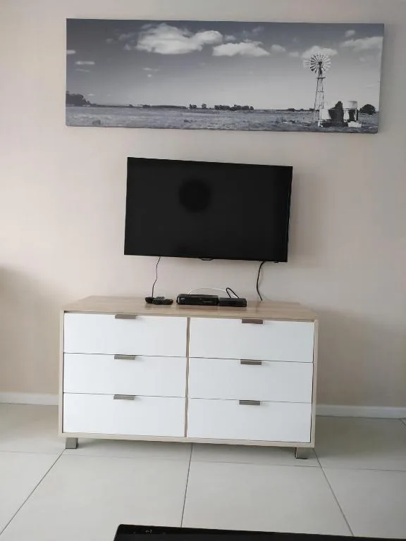 Modern lounge with mounted TV above white dresser and countryside artwork