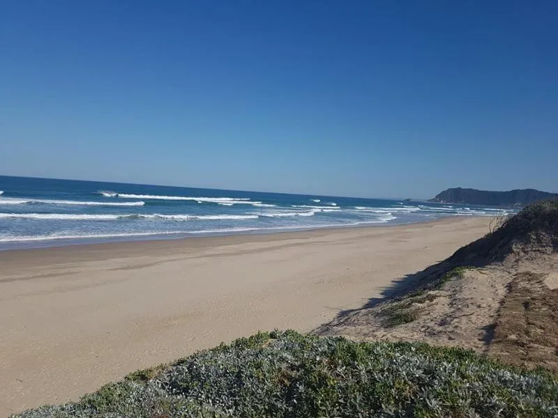 Wide sandy beach with rolling waves and distant coastal hills under clear blue sky