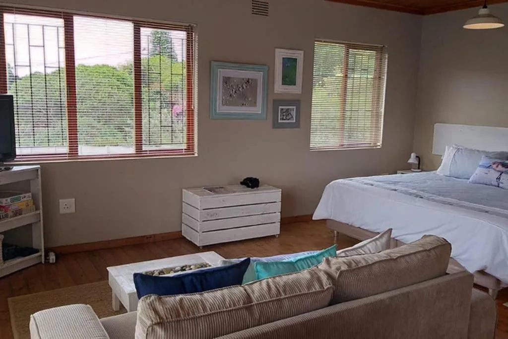 Spacious bedroom with queen bed, windows overlooking garden, and lounge seating area