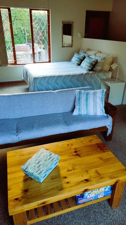Bright bedroom with queen bed, blue upholstered sofa, wooden table, garden views