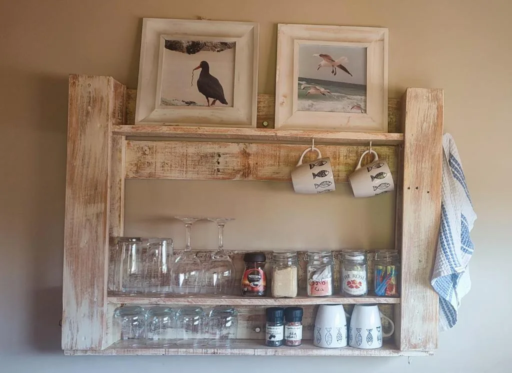 Rustic wooden wall cabinet displaying glassware, mugs, and coastal bird artwork