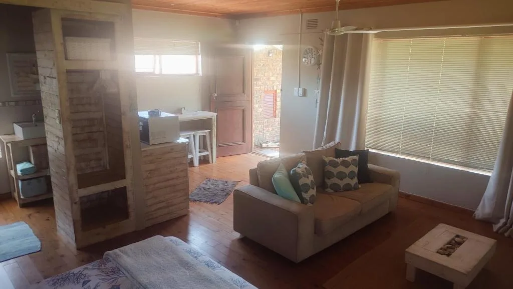 Open-plan living space with brown sofa, wooden floors, and bright windows