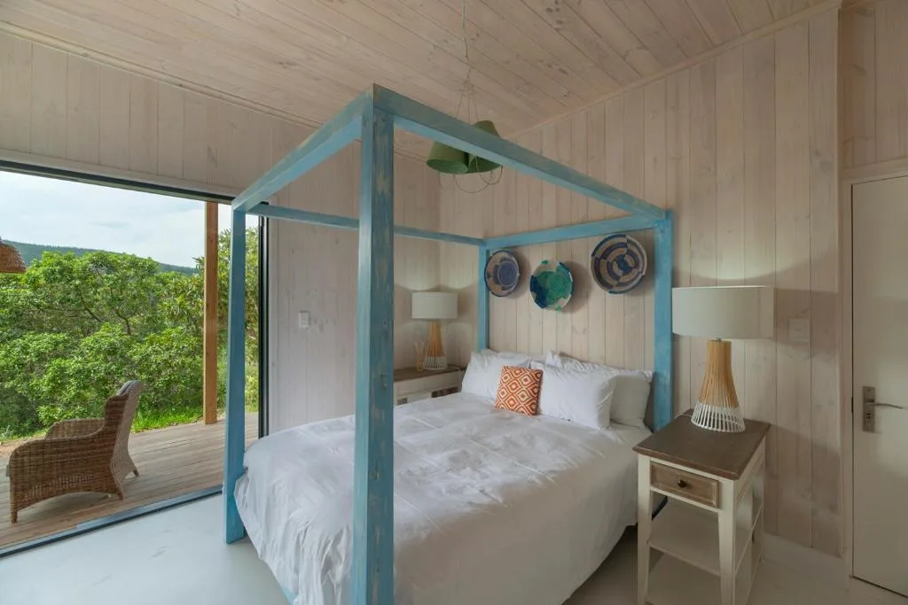 Spacious bedroom with blue four-poster bed and ocean view through glass doors