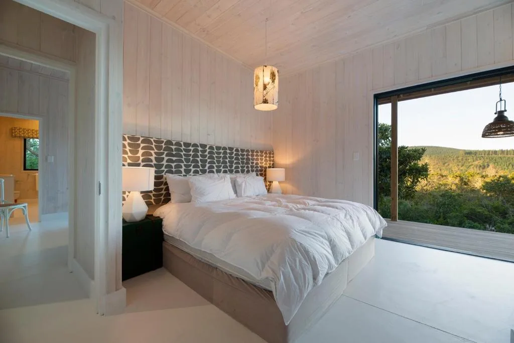 Modern bedroom with white bedding, patterned headboard, and garden views through sliding doors
