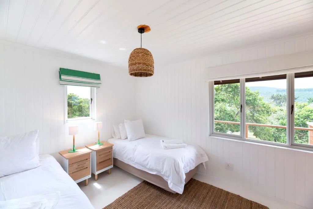 Bright bedroom with twin beds, wooden nightstands, and scenic garden views through windows